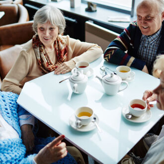 Vier Seniorinnen sitzen an einem mit Kaffeetassen gedeckten Tisch und unterhalten sich angeregt.