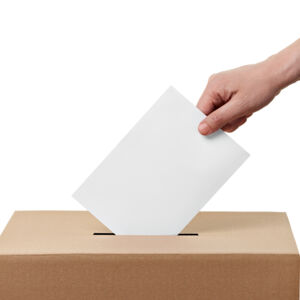 Wahlen Man sieht eine Hand, die einen Zettel in den Schlitz einer Wahlurne steckt