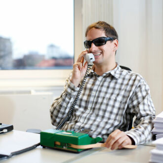 Heiko Kunert sitzt an seinem Schreibtisch und telefoniert. Vor ihm steht seine Punktschrift-Stenomaschine für Notizen