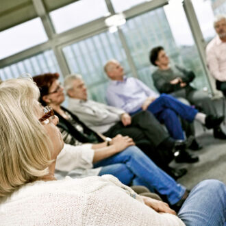Eine Gruppe Menschen sitzt in einem Stuhlkreis. Die Menschen richten ihre Aufmerksamkeit auf etwas - vermutlich einen Redner - außerhalb des Bildes