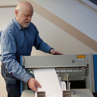 Norbert Antlitz holt ein Dokument aus dem Punktschriftdrucker. Er fertigt im Auftrag barrierefreie Dokumente für Menschen mit Seheinschränkungen an.