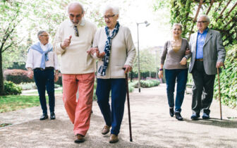 Eine Gruppe Senioren und Seniorinnen geht paarweise mit Spazierstöcken und miteinander untergeharkt spazieren.