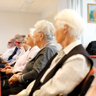 Eine Reihe Senioren und Seniorinnen sitzt an einer langen gedeckten Kaffeetafel. Sie nehmen am Seniorennachmittag im Louis-Braille-Center teil.