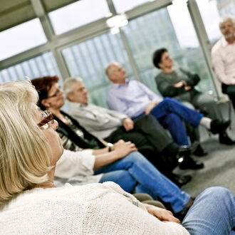 Eine Gruppe Menschen sitzt in einem Stuhlkreis. Die Menschen richten ihre Aufmerksamkeit auf etwas - vermutlich einen Redner - außerhalb des Bildes