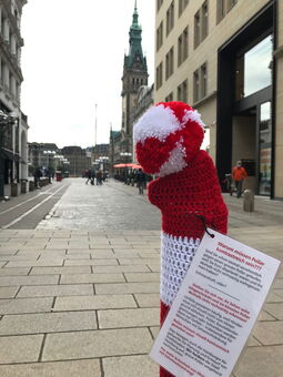 Ein Poller mit einer Pollermütze mit Info-Faltblatt im Vordergrund. Im Hintergrund der Rathausmarkt und das Rathaus