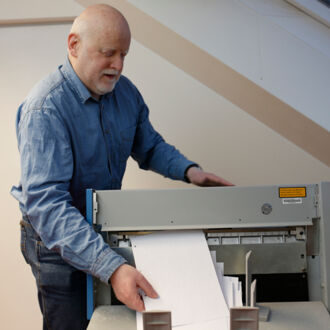 Norbert Antlitz holt ein Dokument aus dem Punktschriftdrucker. Er fertigt im Auftrag barrierefreie Dokumente für Menschen mit Seheinschränkungen an.