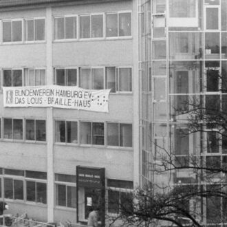 Eine historische Abbildung vom Holsteinischen Kamp 26. Am Gebäude hängt ein Transparent mit dem damaligen Vereinsnamen "Blindenverein Hamburg e.V. - Das Louis-Braille-Haus". Das Bild stammt aus dem jahr 1988