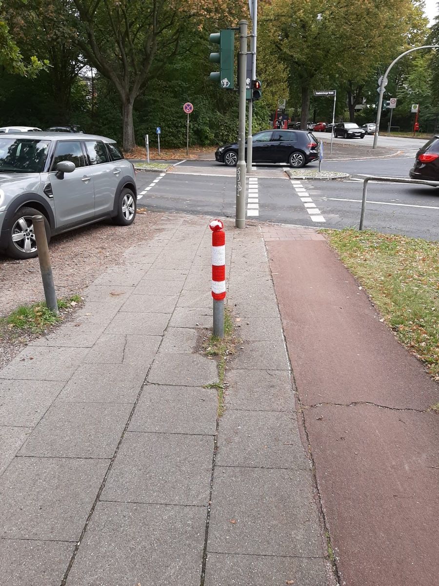 Grauer Straßenpoller in Eilbek mit rot-weiß-gesteifter Strichmütze