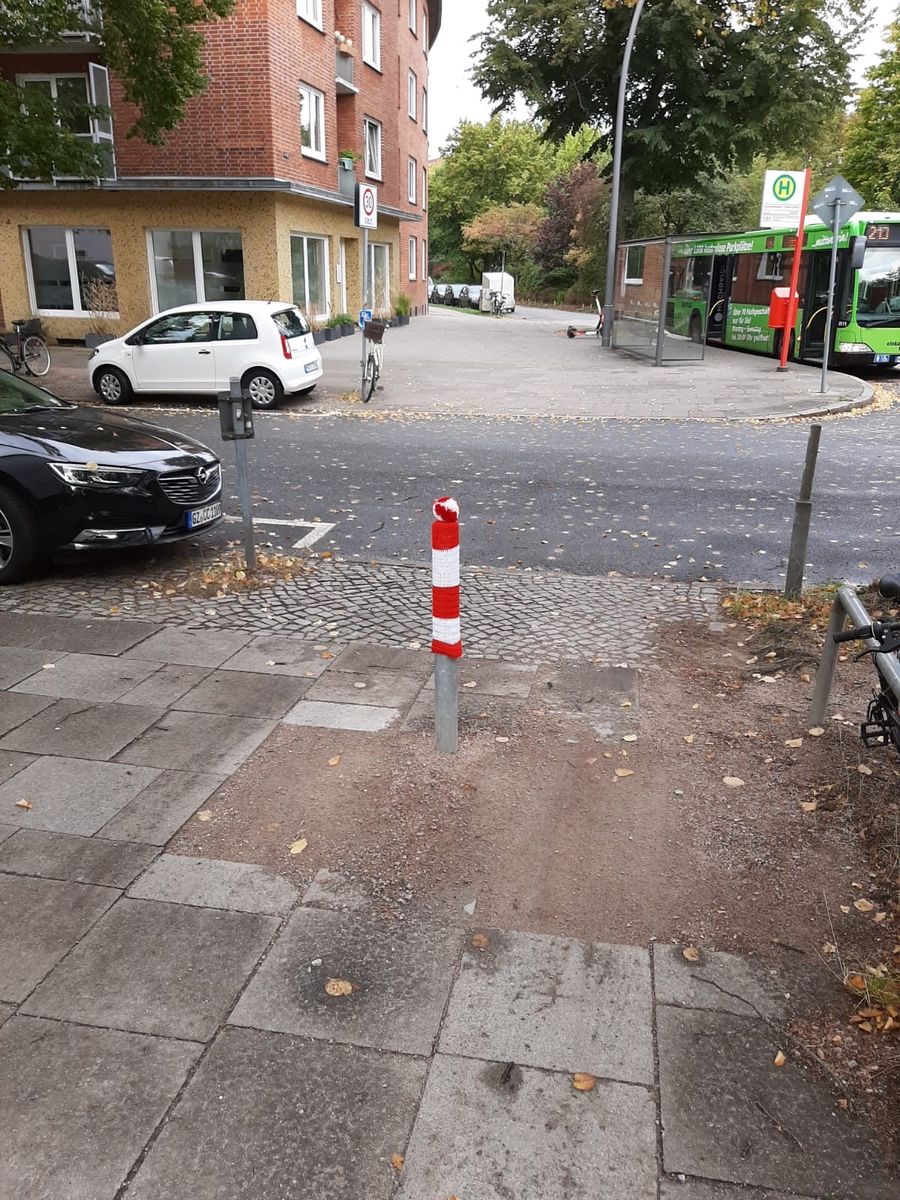 Grauer Straßenpoller in Eilbek mit rot-weiß-gesteifter Strichmütze