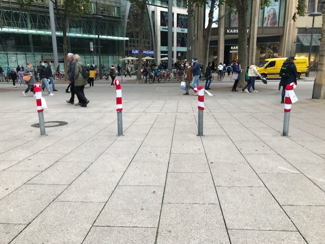 Graue Straßenpoller in der Innenstadt mit rot-weiß-gestreiften Strickmützen