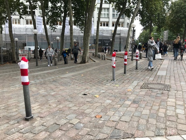 Graue Straßenpoller in der Innenstadt mit rot-weiß-gestreiften Strickmützen